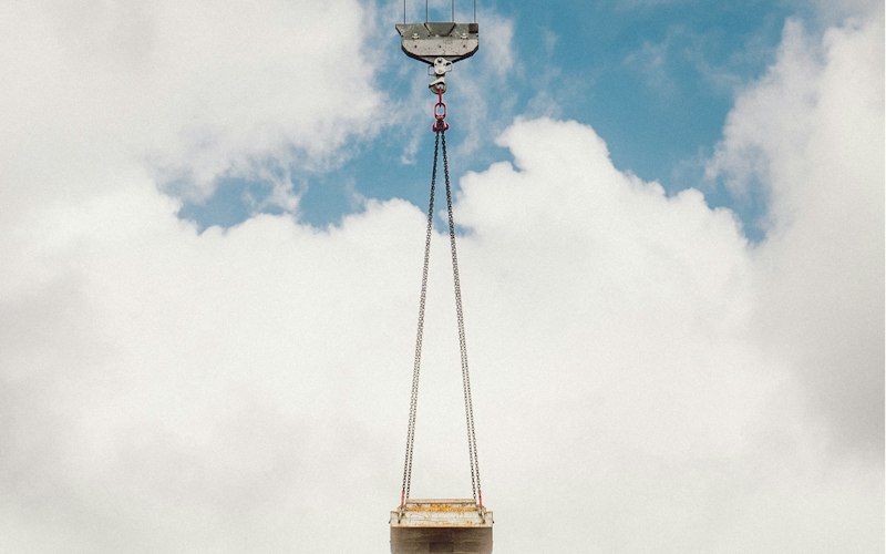 Overhead crane hook lifting a steel load against the sky
